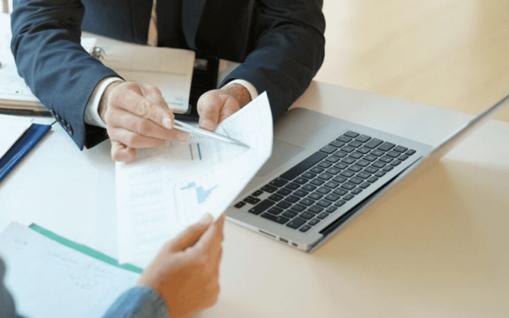 Business professionals discussing hard cash money loans at a desk with a laptop, documents, and charts, represent DeNovus Capital's services.